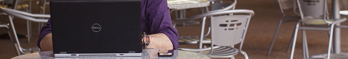 A person typing on a laptop while sitting at an outdoor table