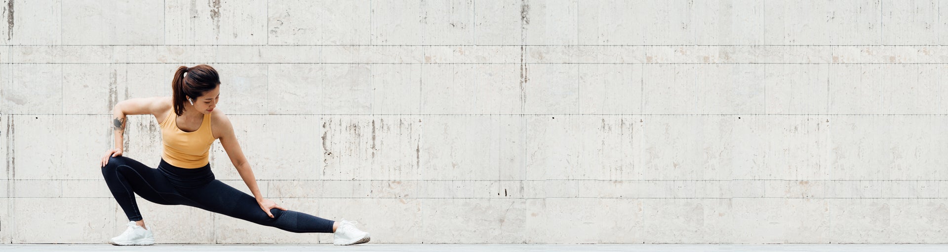 Woman in workout clothes stretching in front of gray-white background