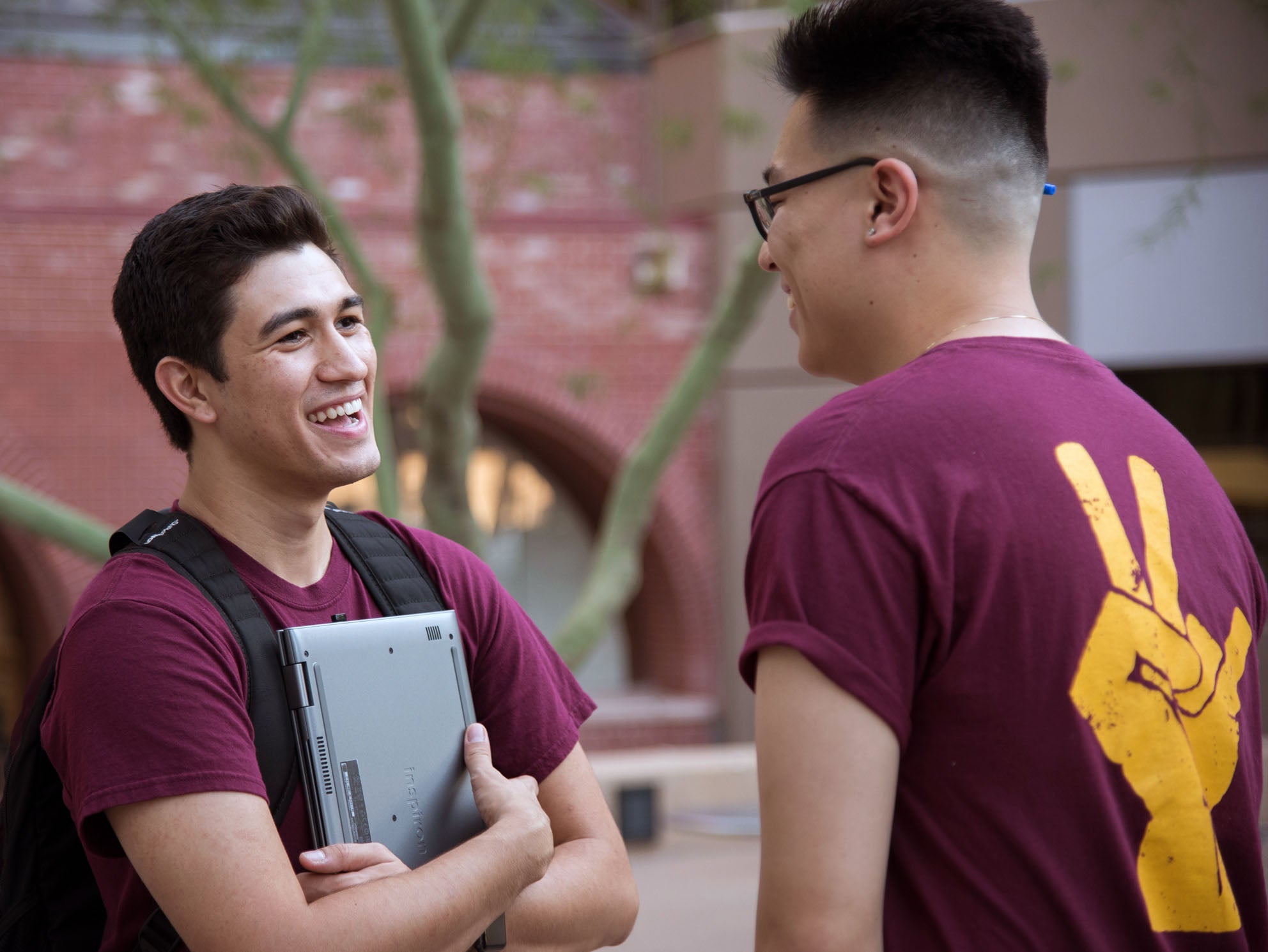 Two male students smiling, one holding a closed laptop