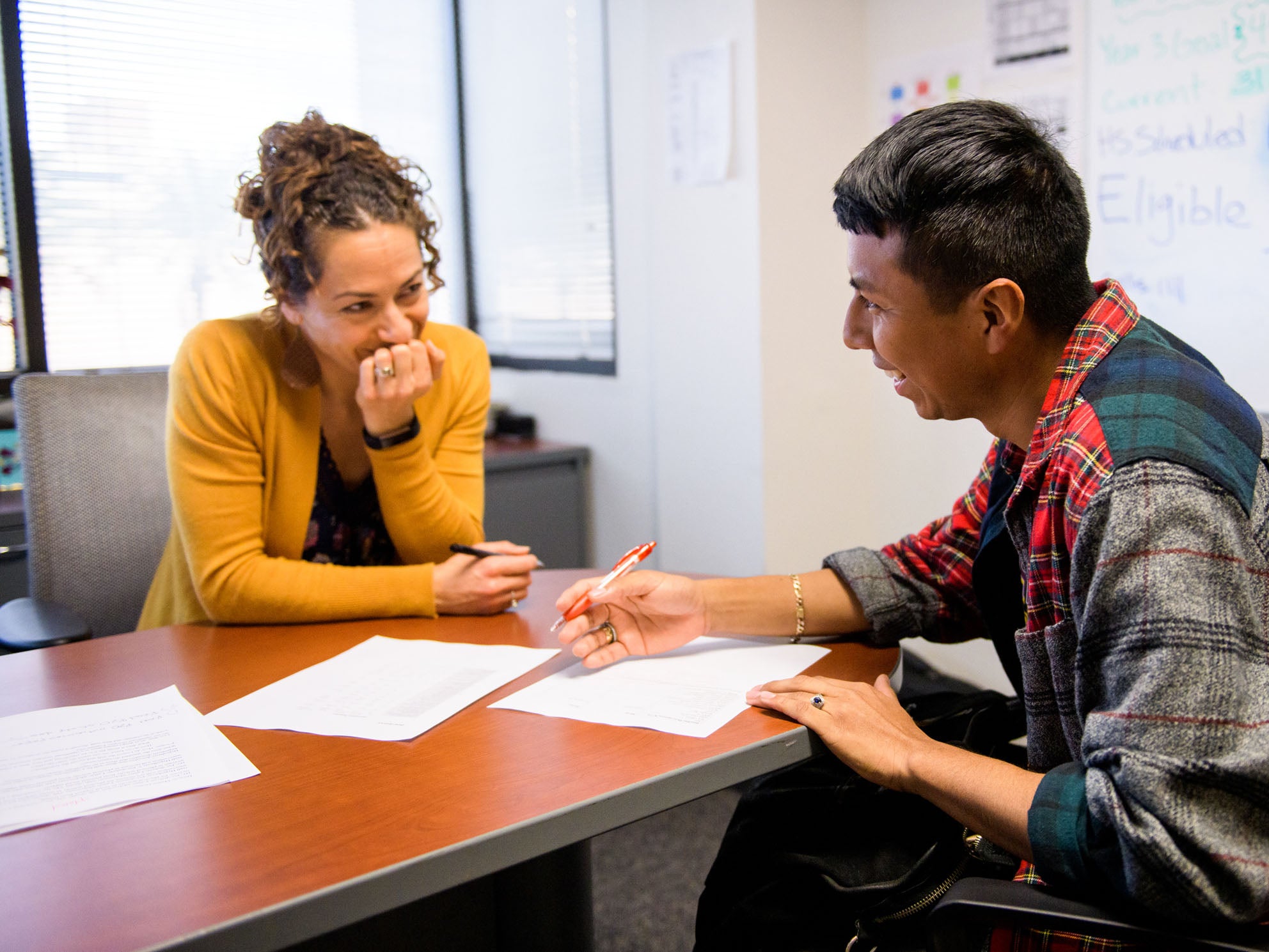 A student completing paperwork at a staff member's desk