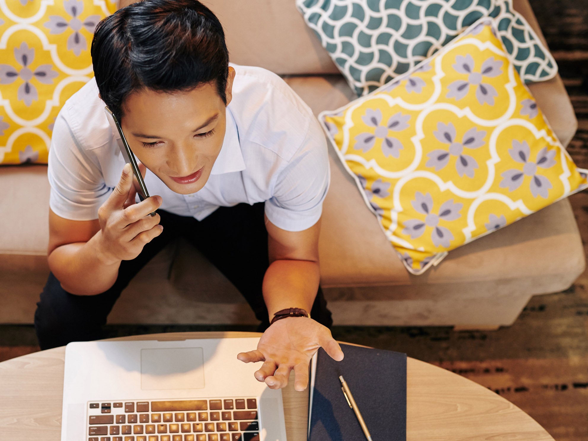 A view from above of a man on a phone sitting in front of a laptop