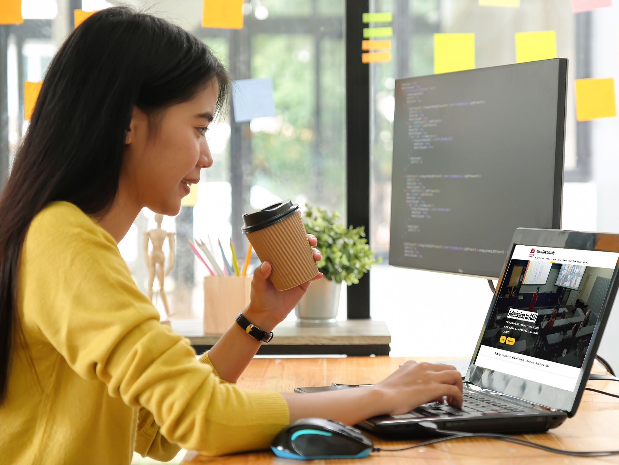 A woman working at a laptop while holding a coffee cup