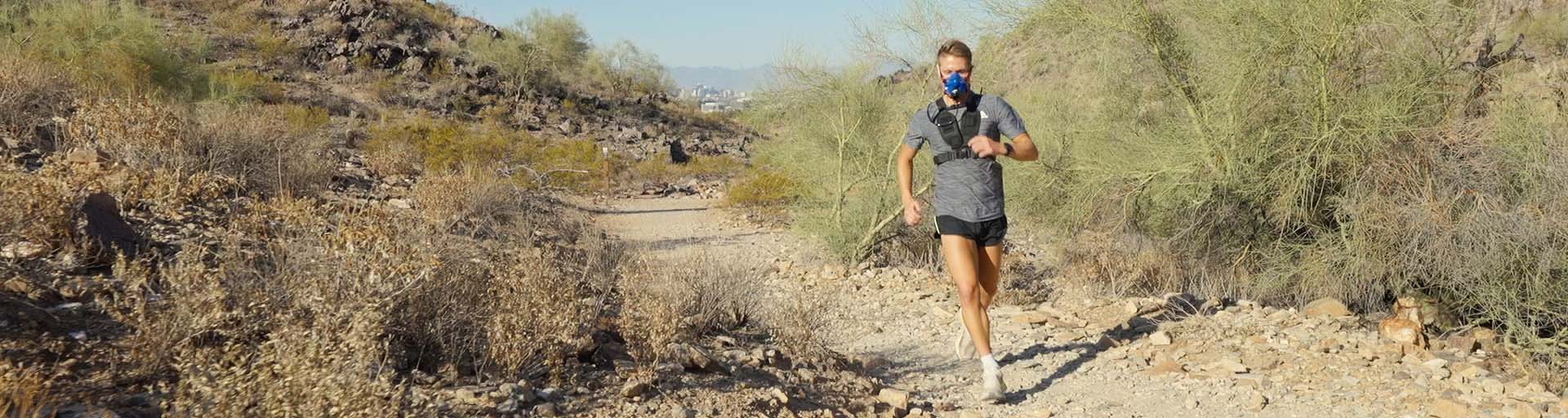 Man running on desert trail with greenery and sky in the background