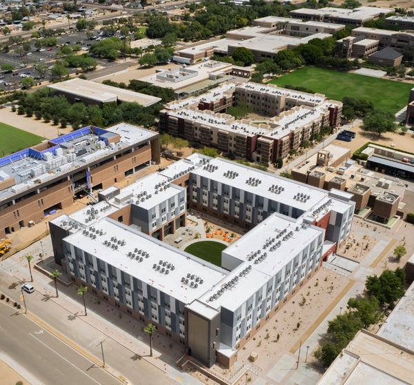 Aerial view of ASU West Valley campus with a large U-shaped building in the foreground and various other structures and a green field in the background.